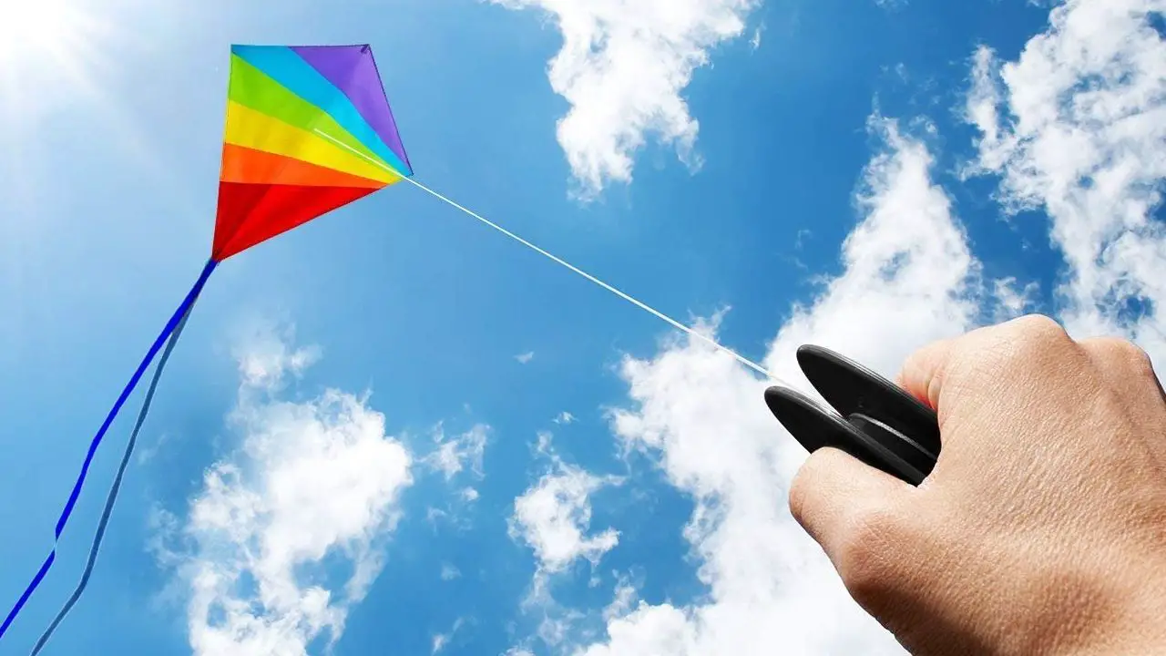 Article image showing somebody holding a kite handle with a diamond kite flying in blue sky with clouds